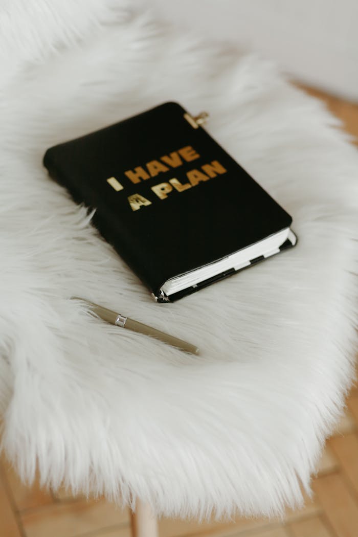 Stylish home office setup featuring a notebook with I HAVE A PLAN text and a pen on a fluffy white chair.